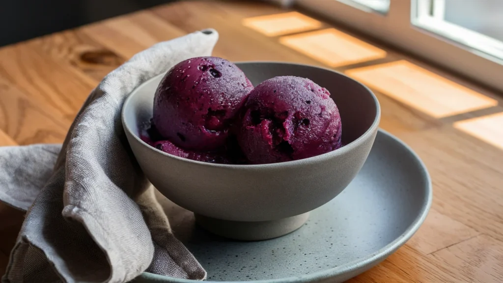 A matte grey ceramic bowl holds two scoops of blueberry sorbet.